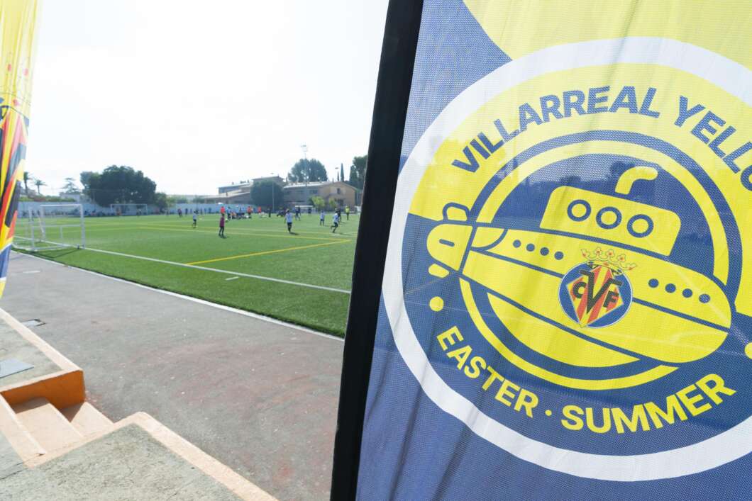 Soccer field with players practicing in the distance; foreground shows a large Villarreal Yellow Submarine banner.