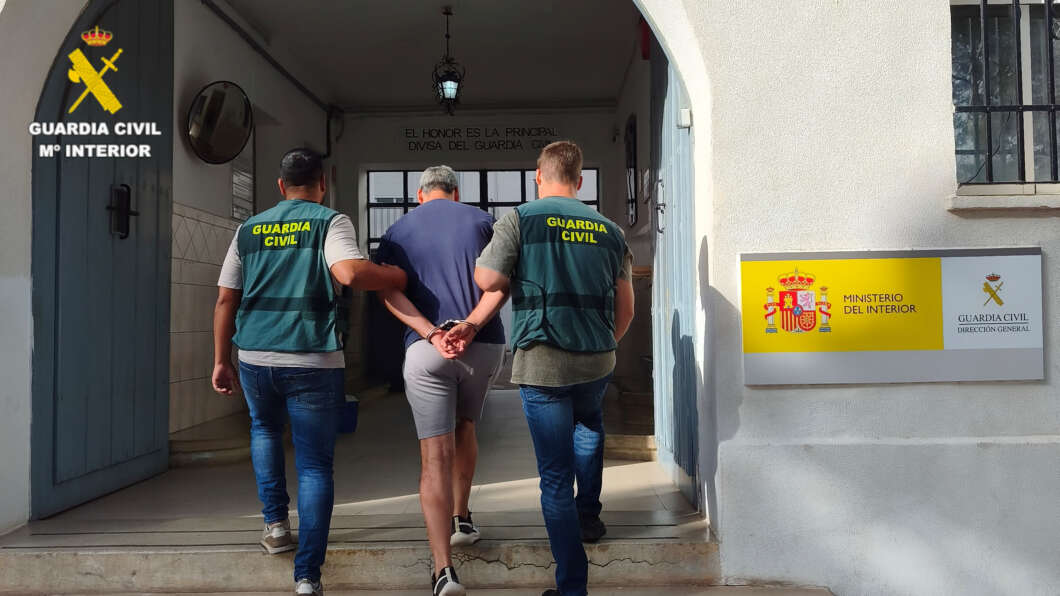 Two Guardia Civil officers escort a handcuffed man into a government building entrance.