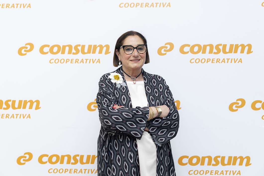 Woman with short hair and glasses stands with arms crossed in front of a wall featuring the 'Consum Cooperativa' logo(s).