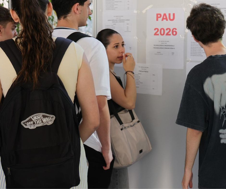 Group of students gathered around posted notices on a wall, with a PAU 2026 sign visible.