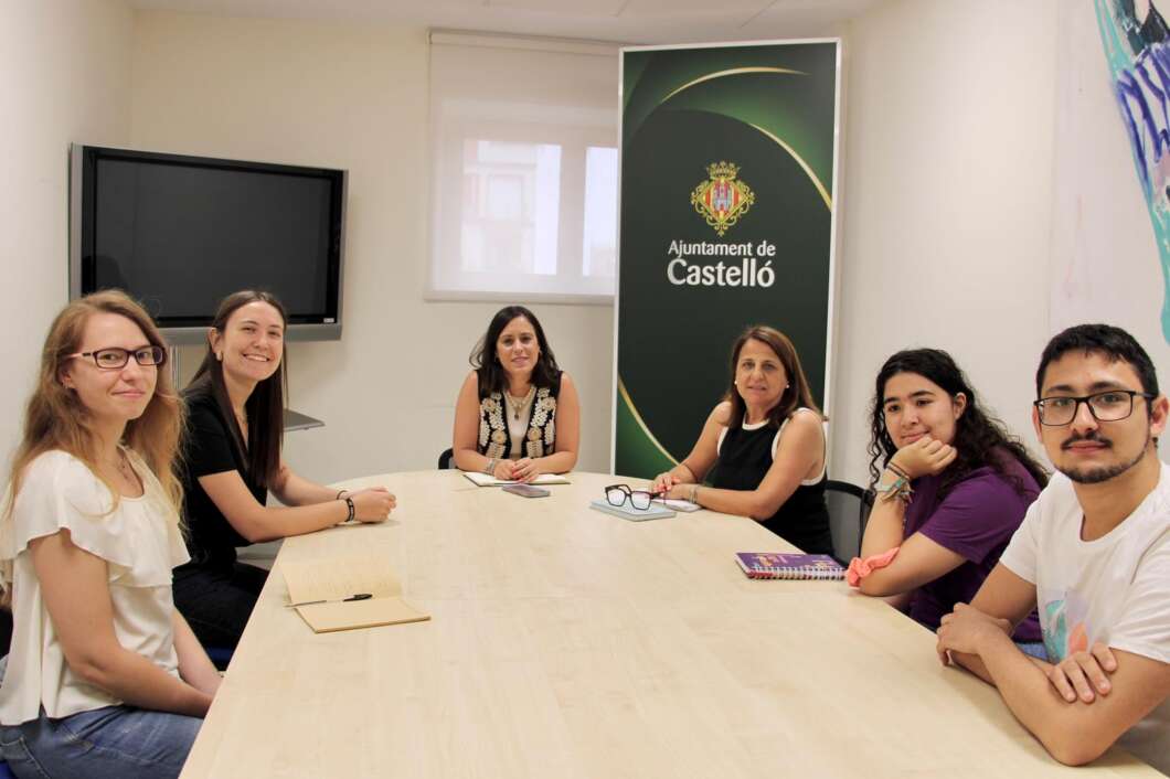 Six people sit around a long light wood conference table in a meeting room, with a 'Ajuntament de Castelló' banner in the background and notebooks on the table.