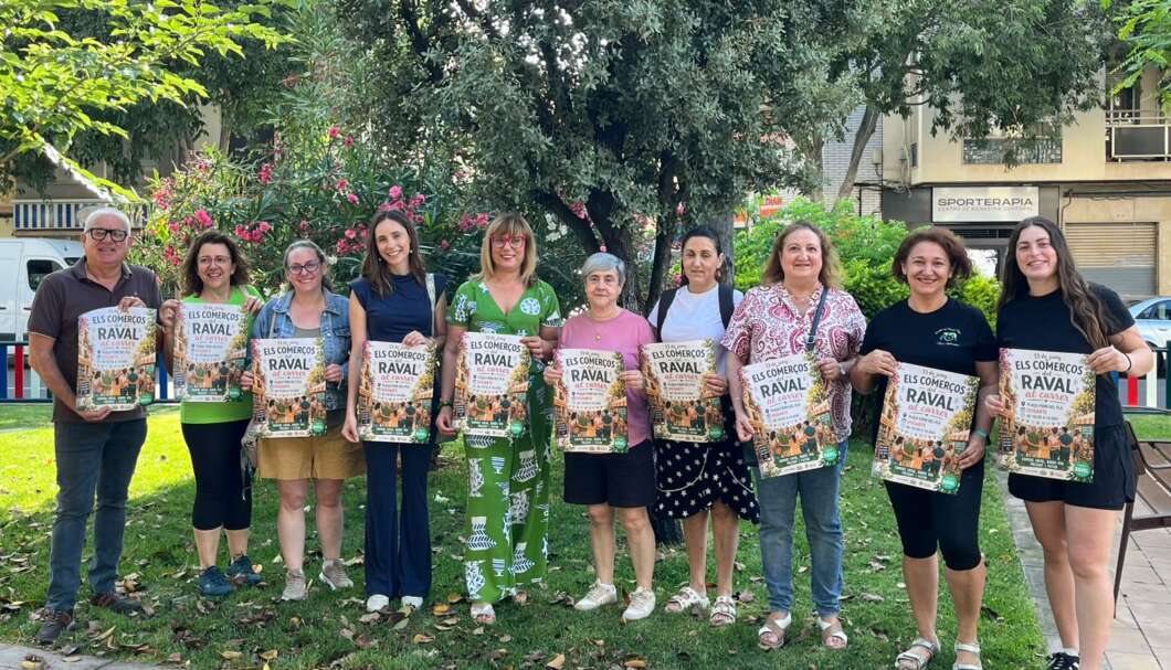 Group of eleven people standing in a park, each holding a poster for 'Els Comerços Raval' event.