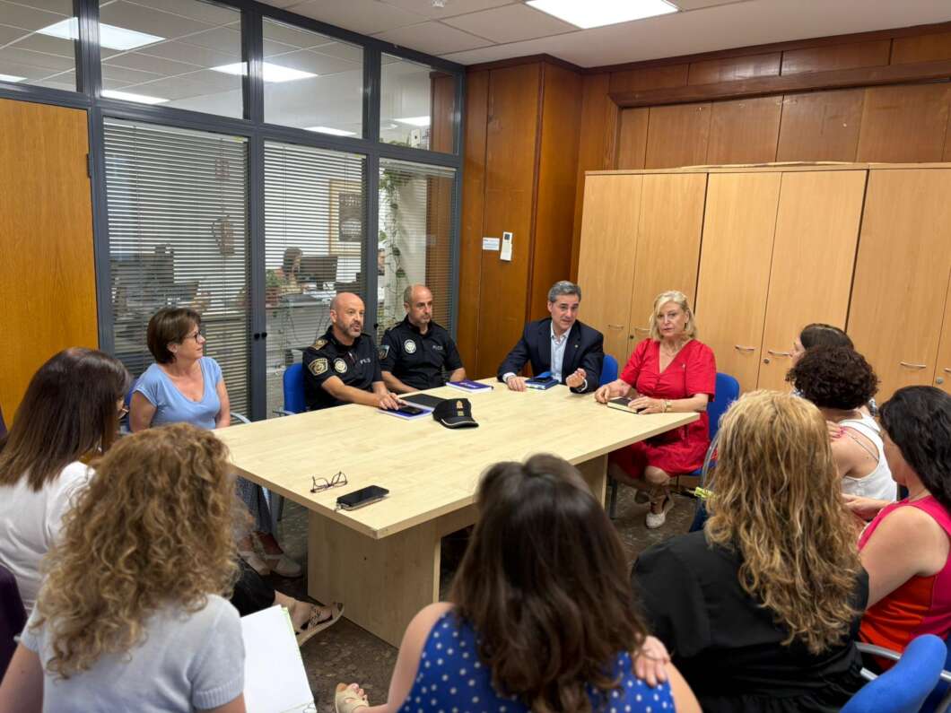 Community meeting in a wood-paneled room; police officers and a man in a suit lead a discussion with civilians around a table.
