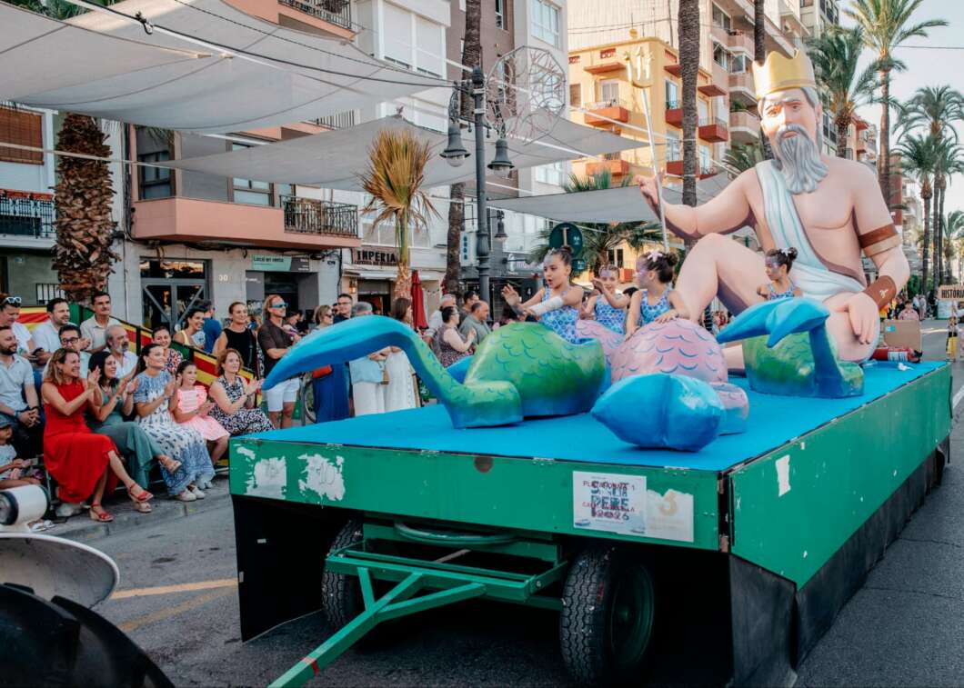 Parade float featuring a large sea god statue and mermaid figures performing while crowds line the street corners.