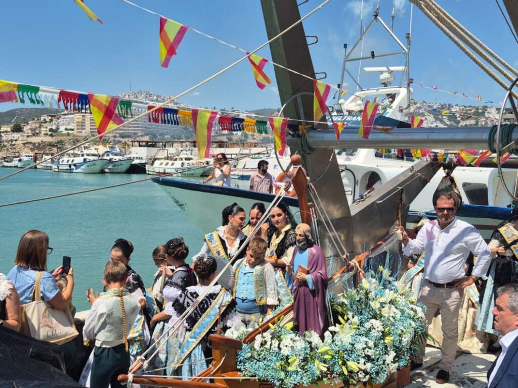 Festival procession on a decorated boat with people in traditional costumes by a harbor. colorful pennants hanging above the water.