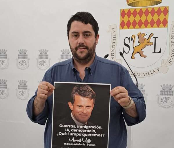 Man wearing a blue shirt holds up a poster with a man's portrait and a Spanish slogan about wars, immigration, AI, democracy, and what Europe we want.