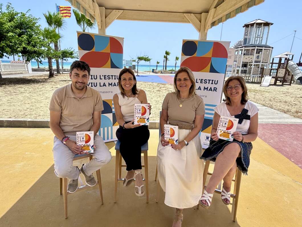 Four adults sit on stools under a beach pavilion, each holding a colorful program booklet with geometric shapes. behind them are banners and a sandy beach.