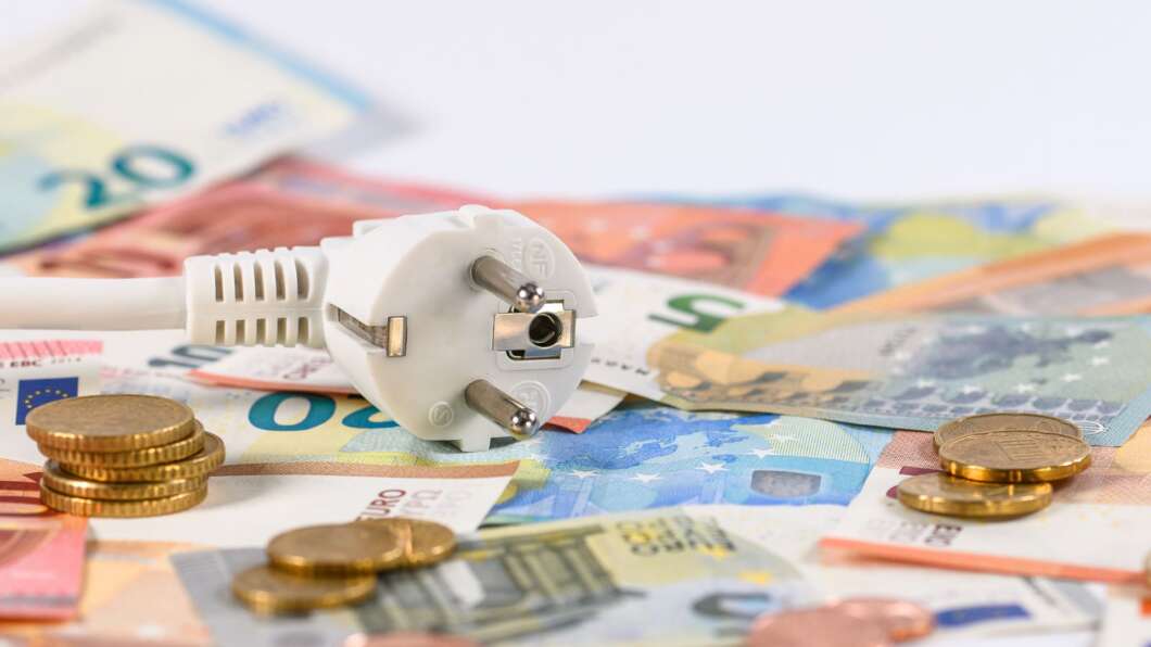 White European plug resting on colorful euro banknotes and coins, symbolizing electricity costs or energy expenses.