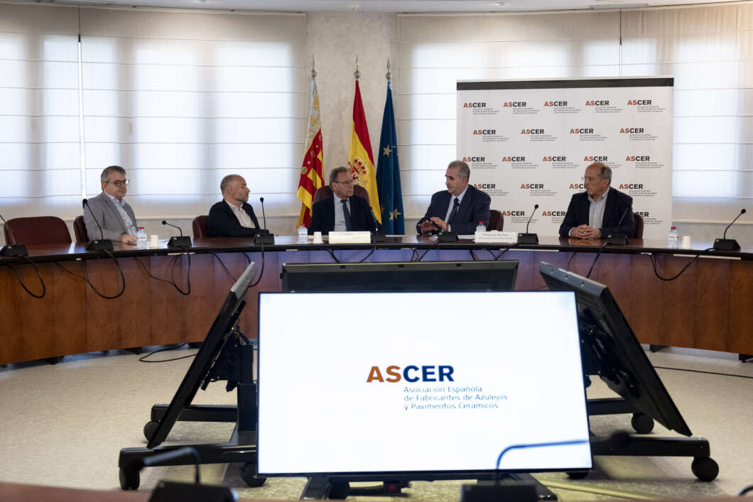 Panel of five men seated at a curved conference table in a meeting room, with flags and an ASCER banner behind, and a large screen in the foreground displaying the ASCER logo.