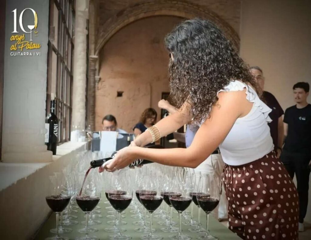 Woman pours red wine into a row of glasses on a table at a wine tasting event.