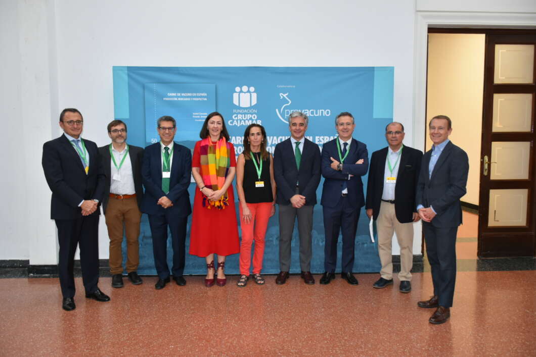 Nine professionals in business attire pose for a group photo in front of a blue event banner with sponsor logos.