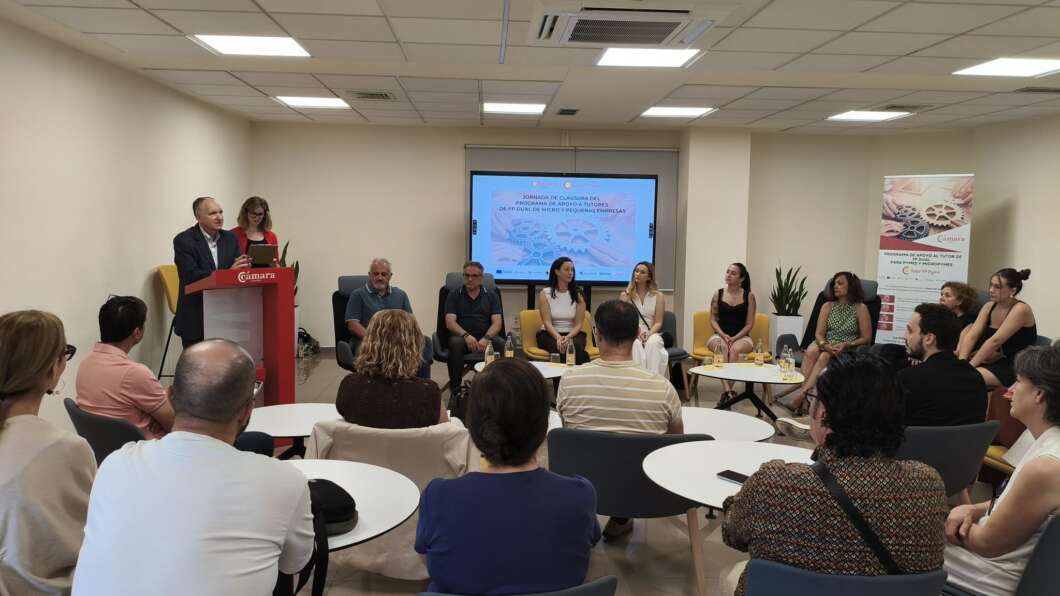 Panel discussion in a bright room with speakers at a red podium on the left and a row of panelists seated near a screen in the back center.