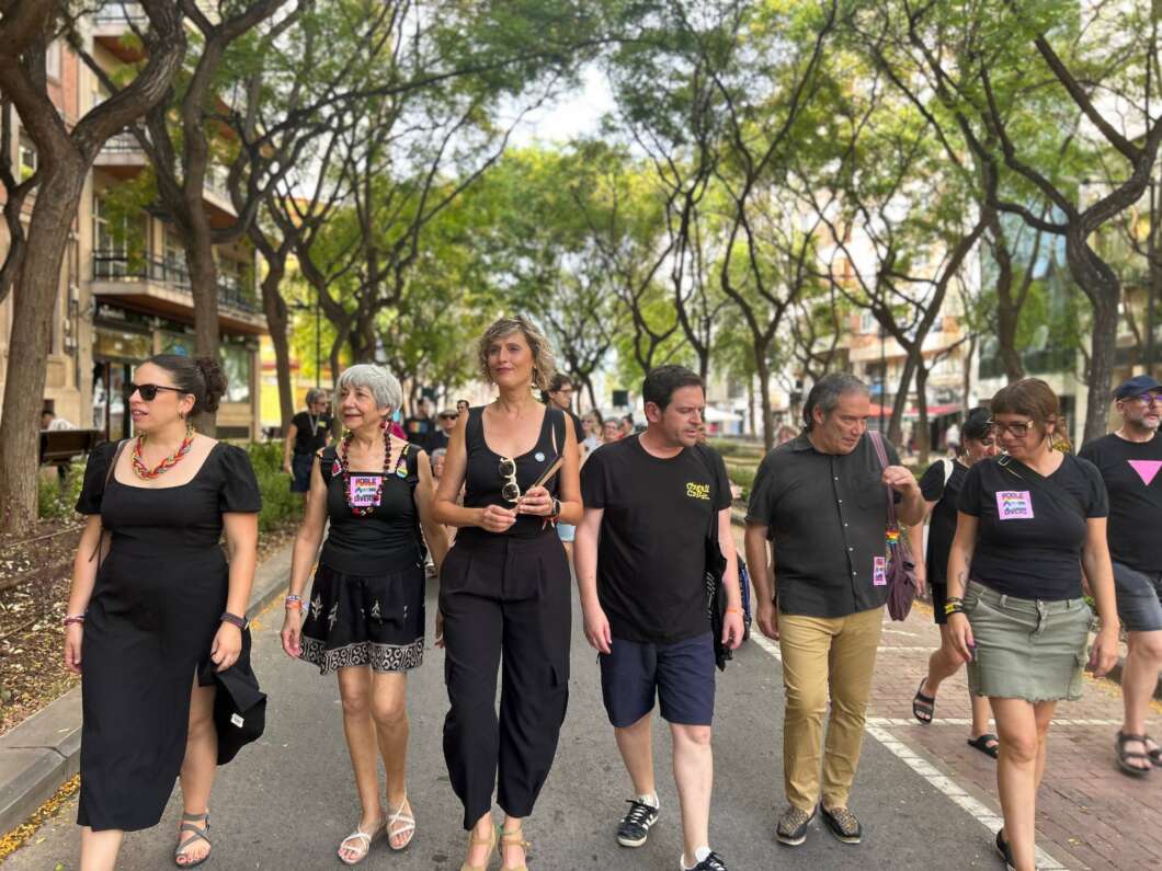 Group of diverse adults walking down a tree-lined city street at an outdoor event, wearing black clothing and badges.