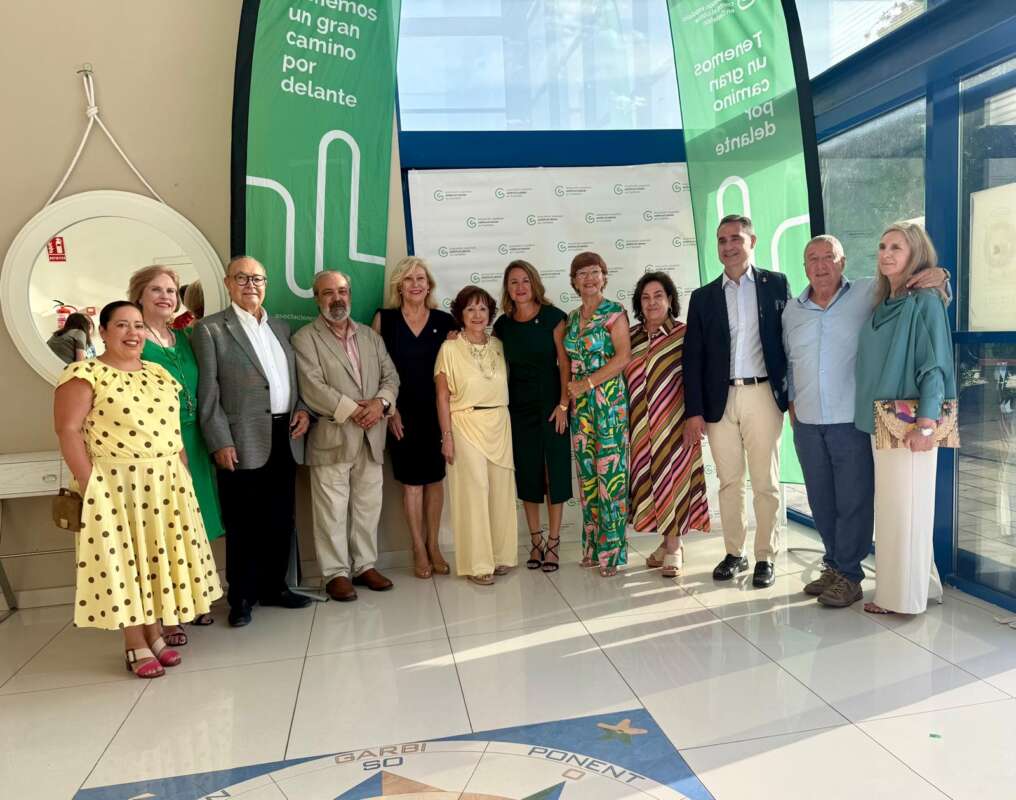 Group of twelve adults in bright lobby posing for a photo; green event banners, glass walls, and a round mirror behind them.