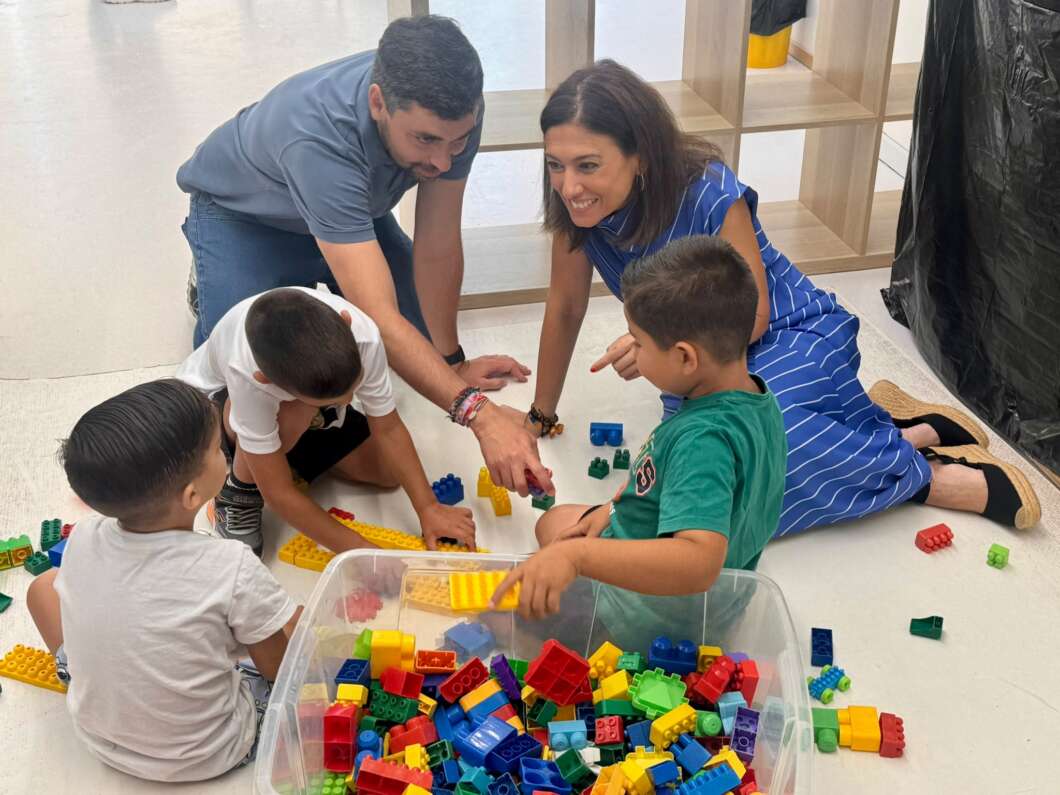 Adults and children sit on the floor playing with colorful Lego-style blocks in a play area.