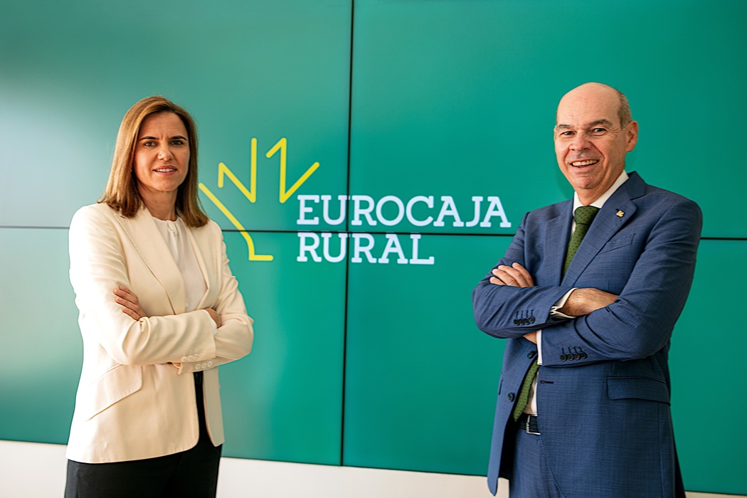 Two professionals, a woman and a man, stand with arms crossed in front of a green wall featuring the Eurocaja Rural logo (corporate photo).