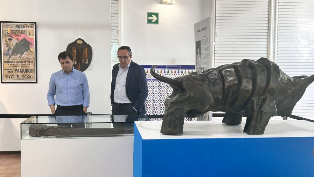 Two men look at a large rhinoceros sculpture on a blue pedestal in a museum.