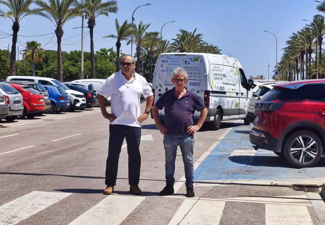 Two men stand on a zebra crosswalk in a sunny parking lot with palm trees, posing for the photo, behind them a white van with logos offers a backdrop.