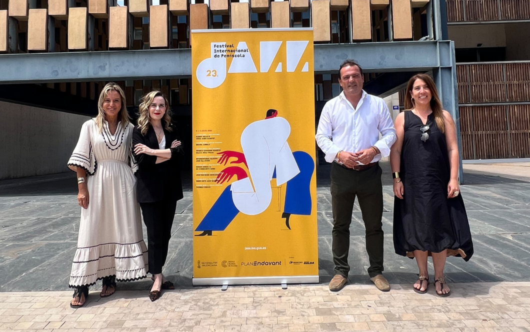 Four adults posing outdoors beside a tall yellow festival banner with abstract artwork and the number 23.