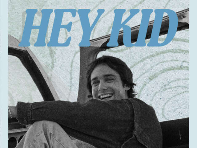Smiling man sits in a car interior with graffiti background; bold blue text 'HEY KID' across the top.