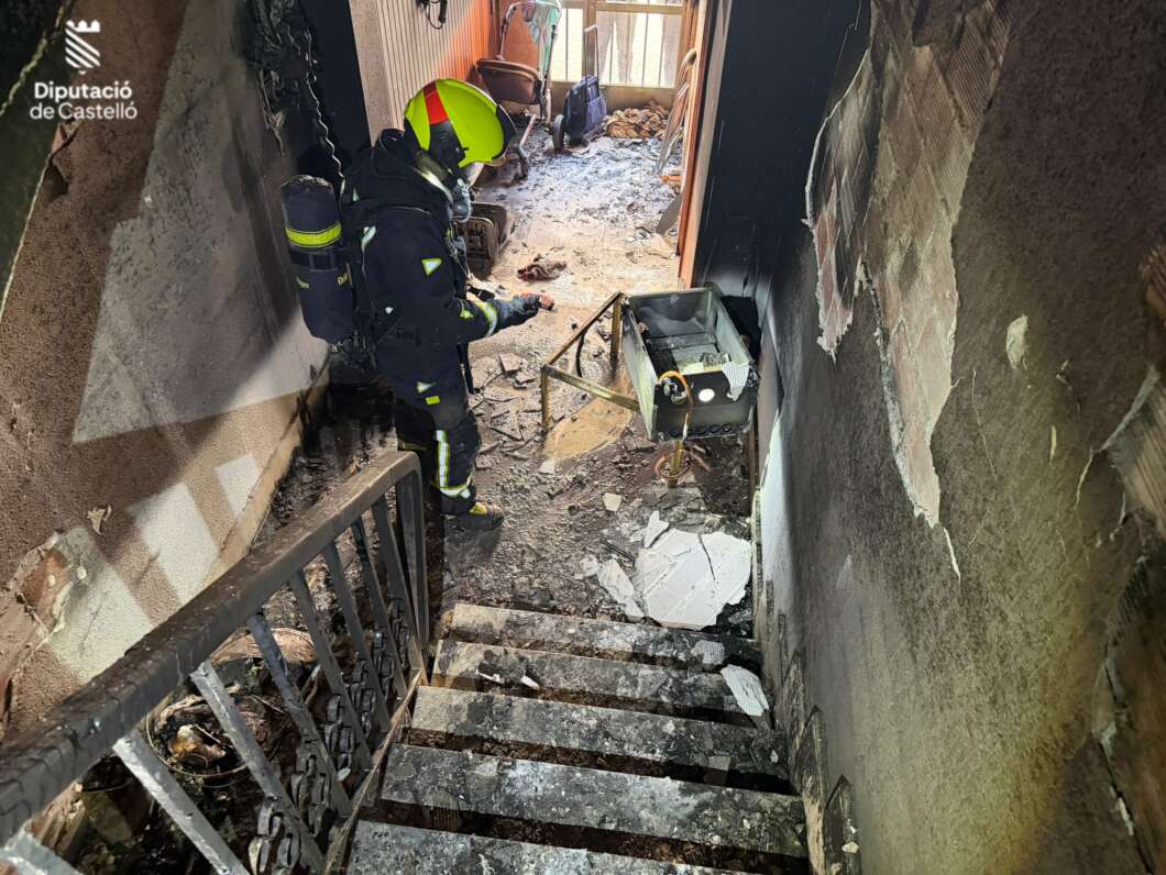 Firefighter in full gear surveys rubble in a burned stairwell; corner shows Diputación de Castellón logo.