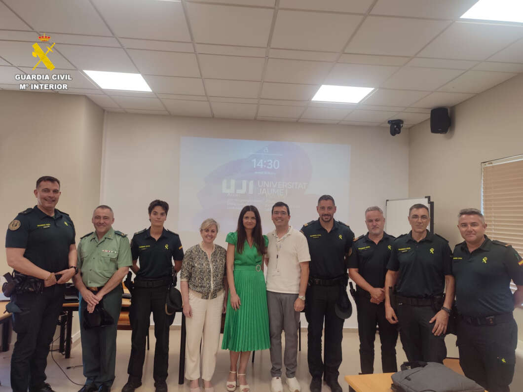 Group photo of Guardia Civil officers and civilians in a classroom or briefing room, posing for a ceremony with a projected logo in the background.