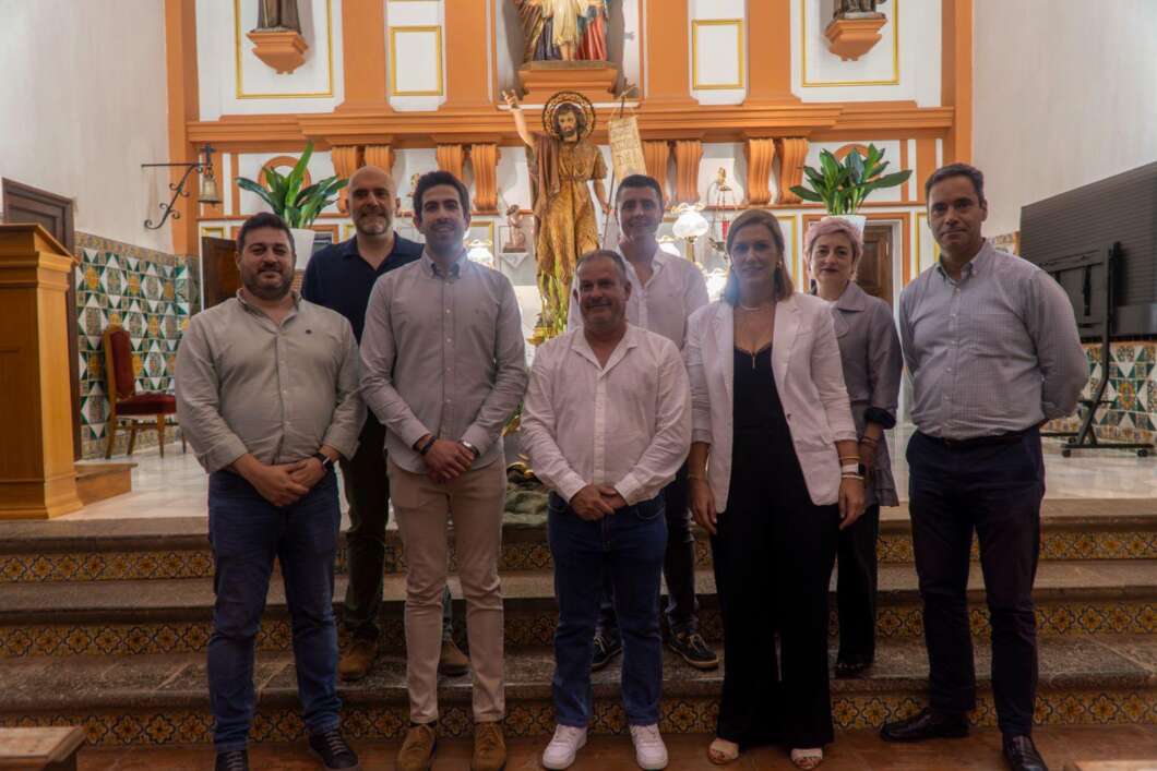 Eight adults pose on church steps in front of an ornate altar and statue, dressed in smart casual attire for a group photo.