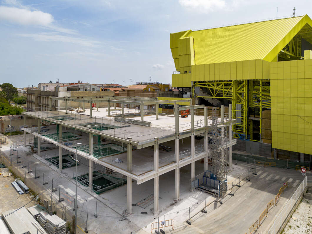 Under-construction multi-story concrete structure beside a bright yellow industrial building.