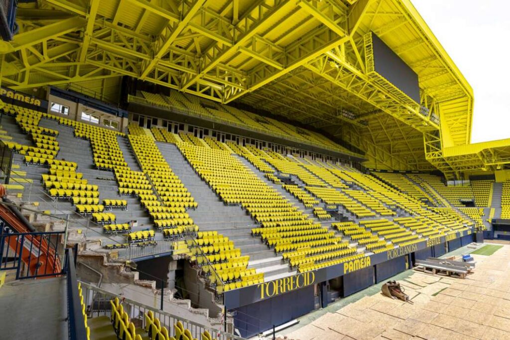 Empty stadium with bright yellow seats and a yellow steel roof structure overhead, giving a vivid, uniform color palette.