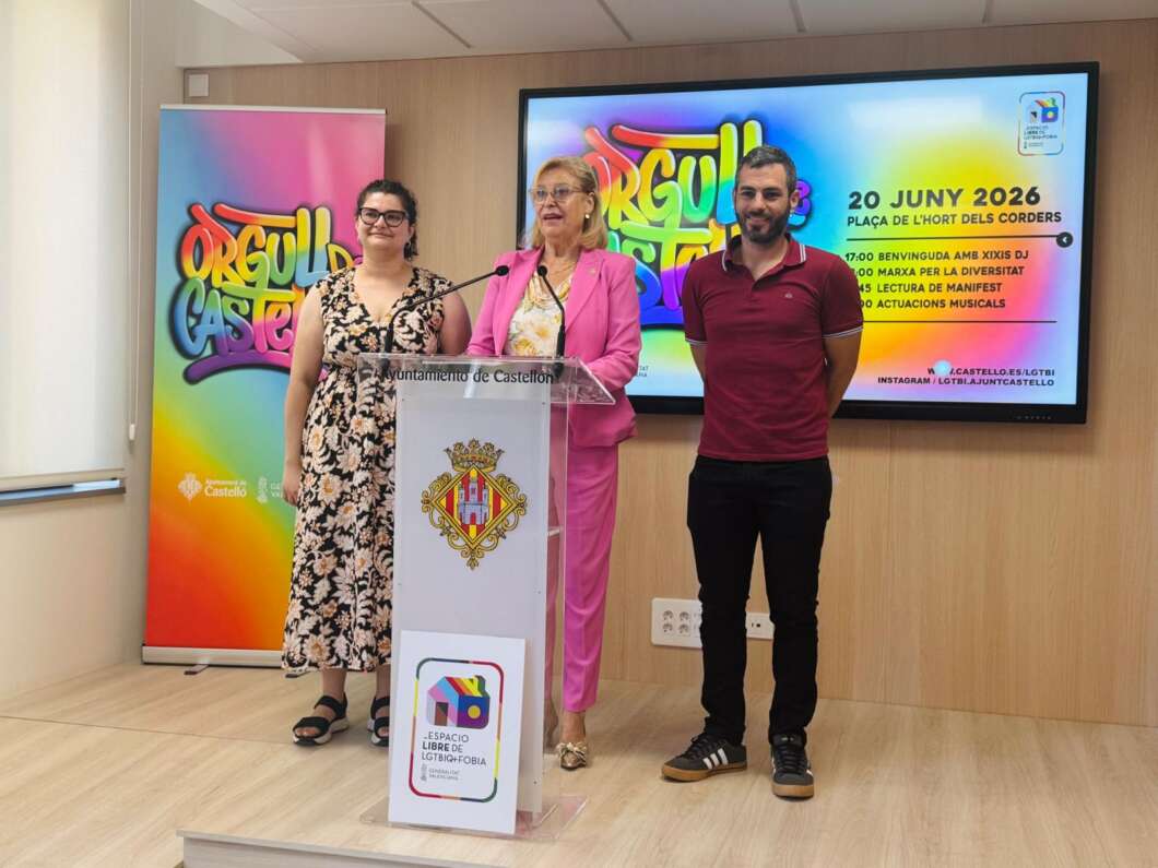 Three adults stand at a clear podium during a community event, with a colorful banner and a large screen behind them.