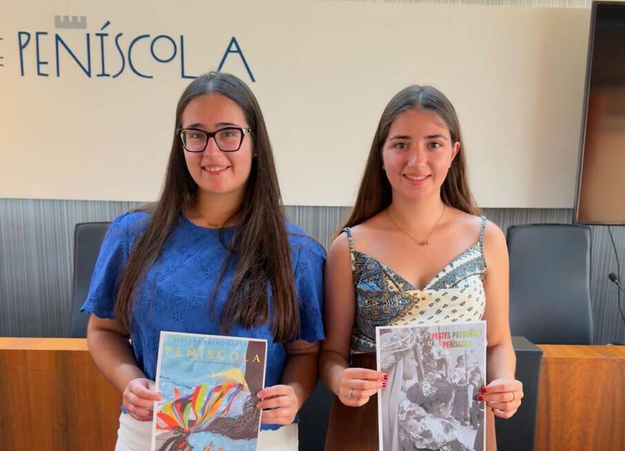 Two young women stand side by side in a conference room, each holding a magazine or brochure in front of them.