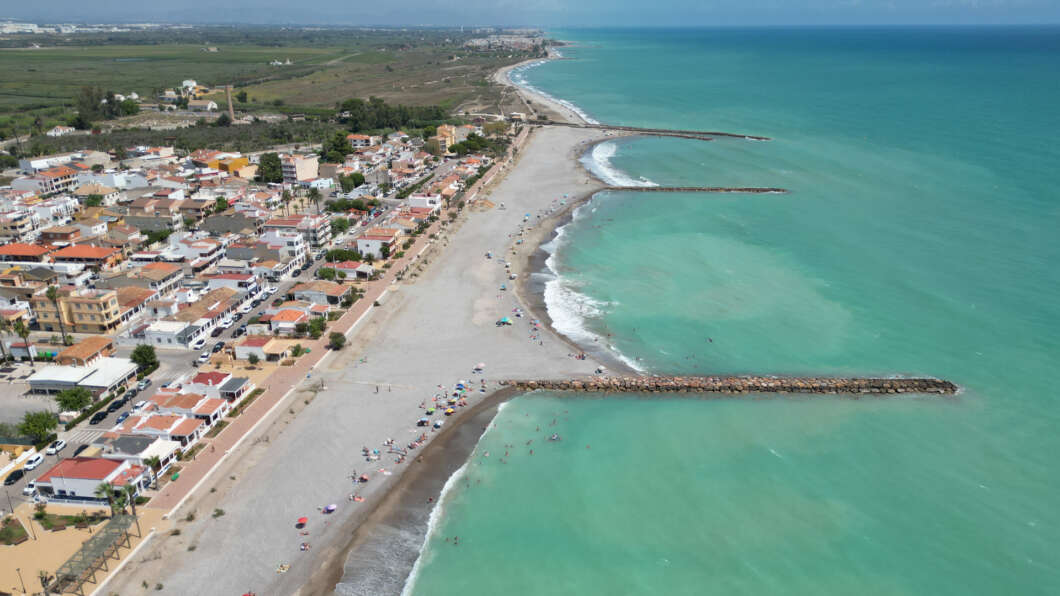 Aerial view of a coastal town with a wide sandy beach, turquoise sea, and two breakwaters extending into the water.