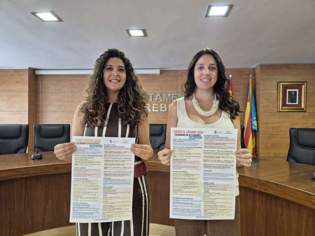 Two women stand in a wood-paneled conference room, each holding a long poster with colored sections.