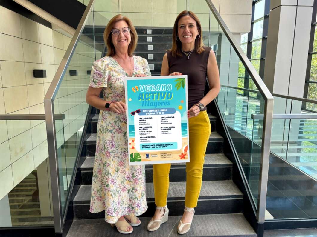 Two women stand on a staircase holding a bright poster about summer activities, smiling at the camera.