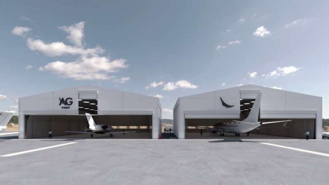Two white aircraft hangars on a tarmac with small private jets inside; a few people stand near the planes under a blue sky with scattered clouds.