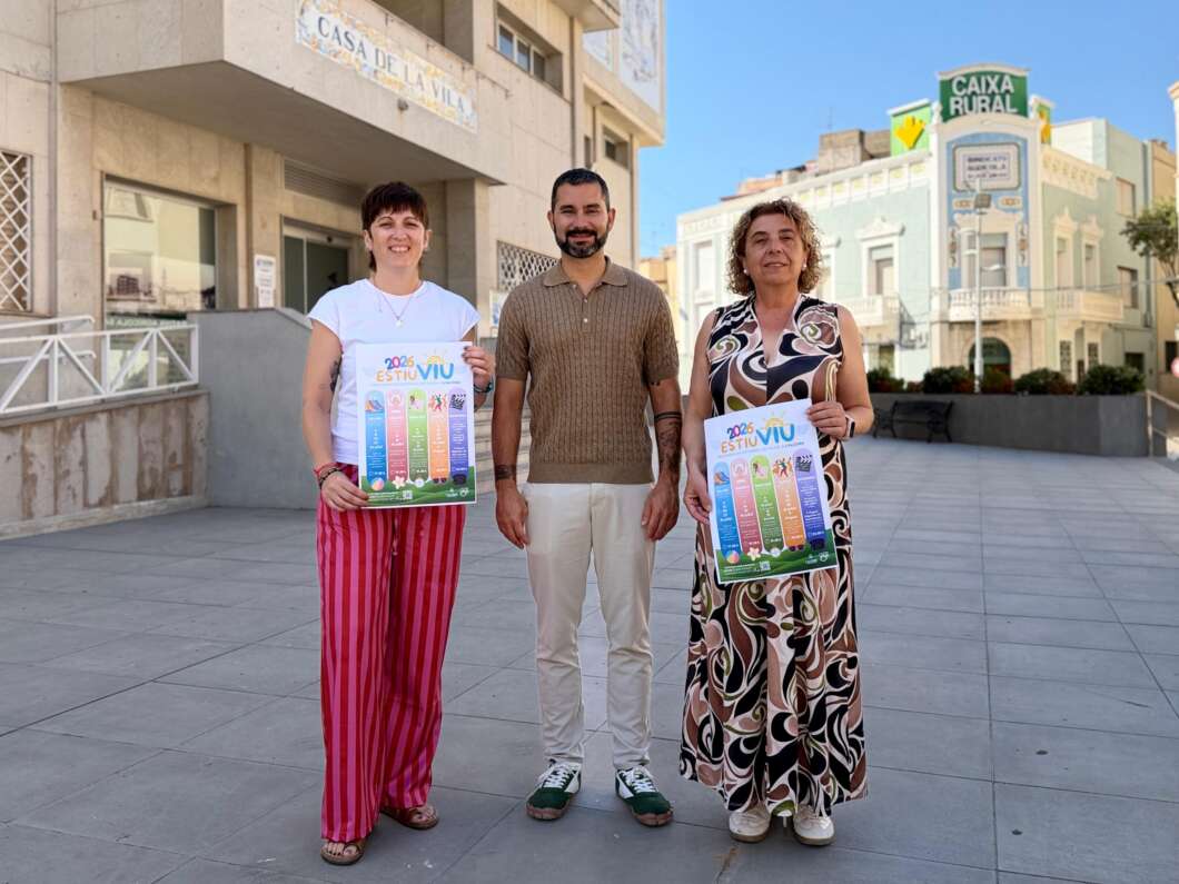 Three adults stand outdoors in a sunny town square, two women and a man, each holding a colorful 2026 Estiu poster.
