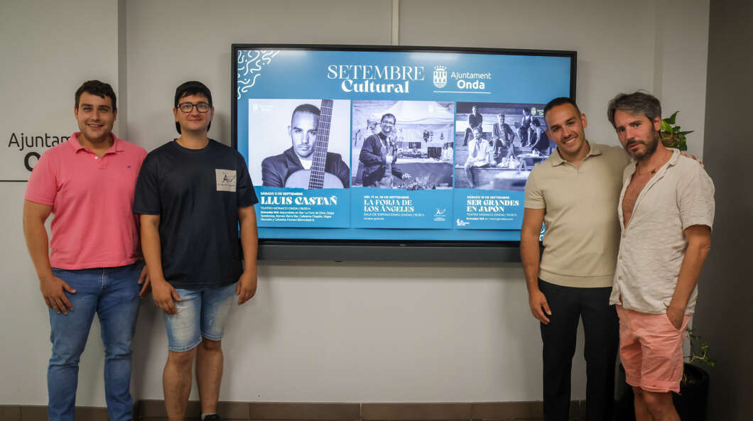 Four men pose in front of a blue Setembre Cultural display at a town hall or municipal building.