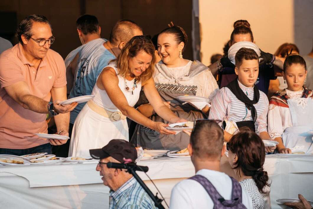 Group of volunteers handing plates of food to guests at a long buffet table during a community meal or charity event.