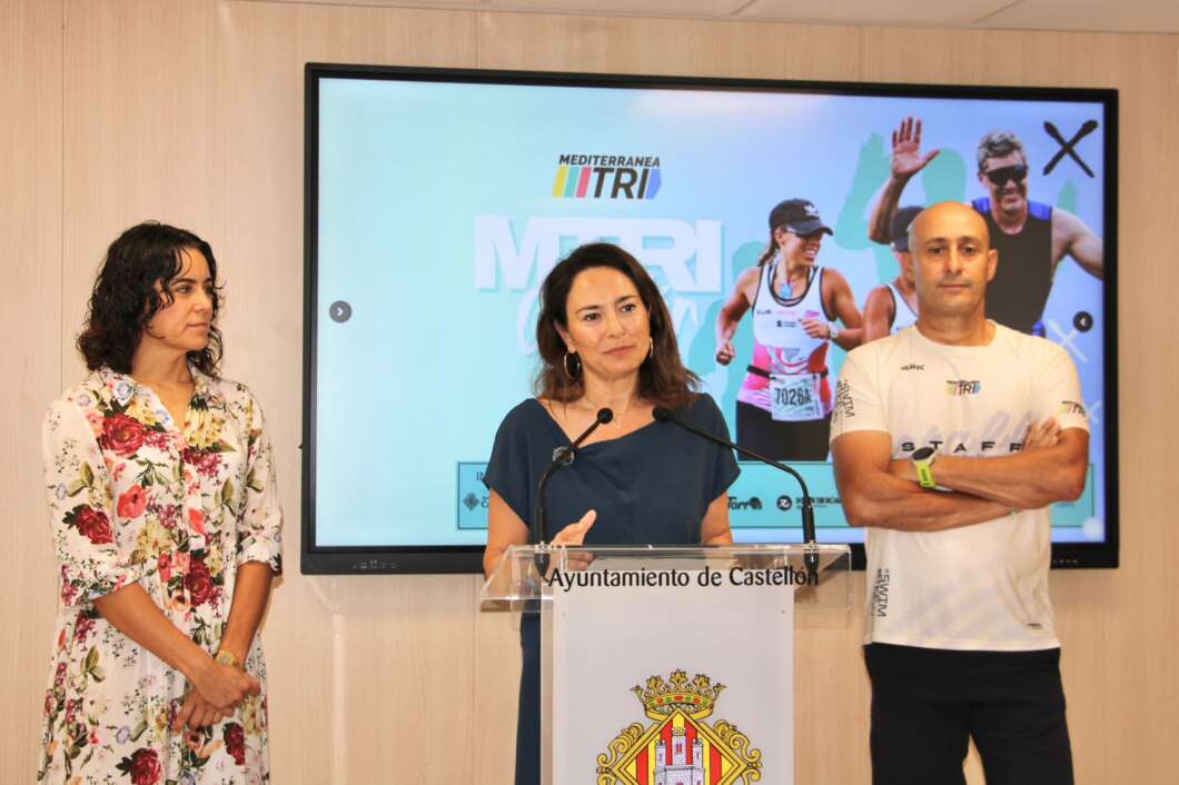 Three people at a podium during a press briefing; center speaker at a lectern with the Ayuntamiento de Castellón crest, a large screen behind them shows athletes and event graphics.