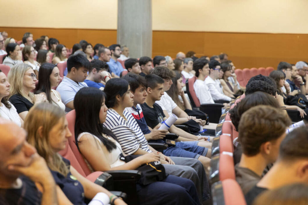 Large audience seated in a lecture hall listening to a presentation in a conference setting.