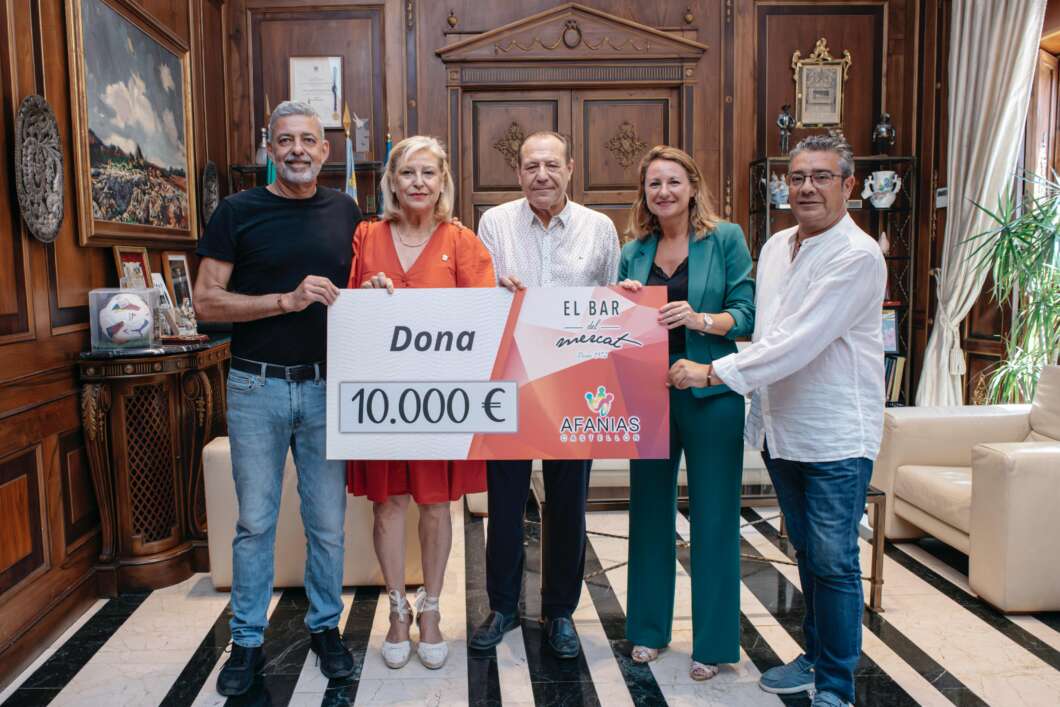 Five adults in a wood-paneled room hold a large 10,000€ donation check for AFANIAS, with 'Dona' visible.
