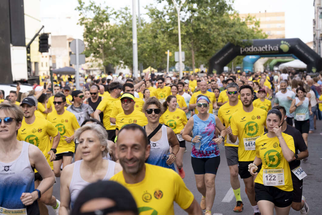 Crowd of runners in a city street race, many wearing bright yellow shirts, with an inflatable arch in the background, daytime.