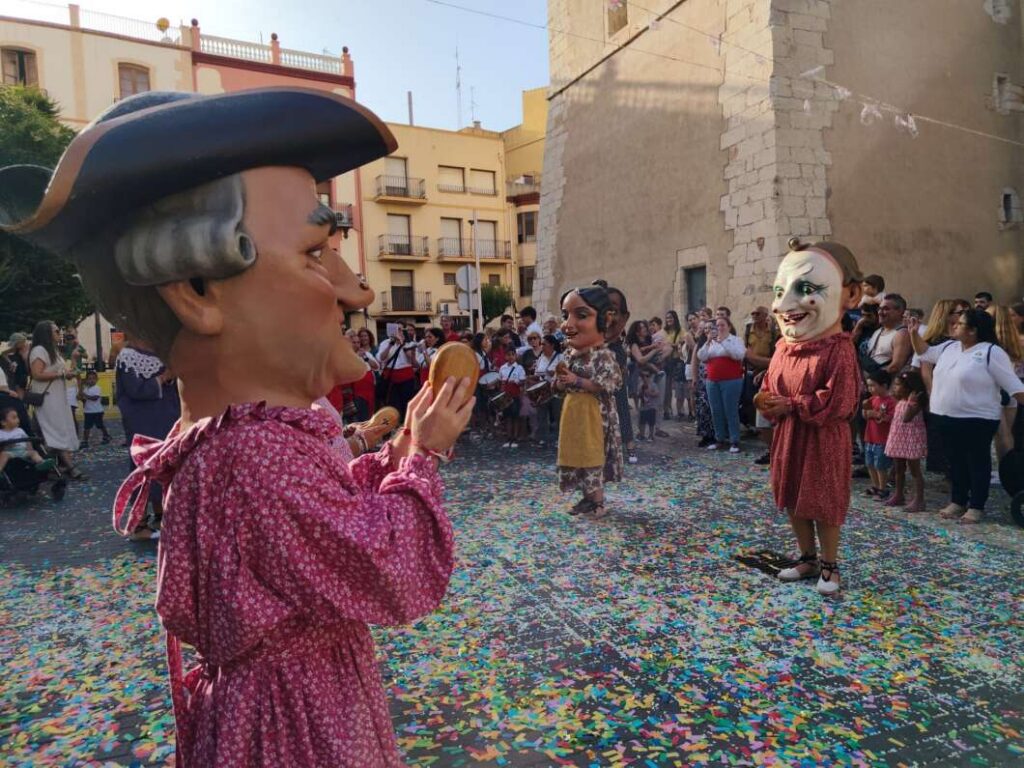 Street festival with giant puppets performing for a crowd as colorful confetti covers the ground.