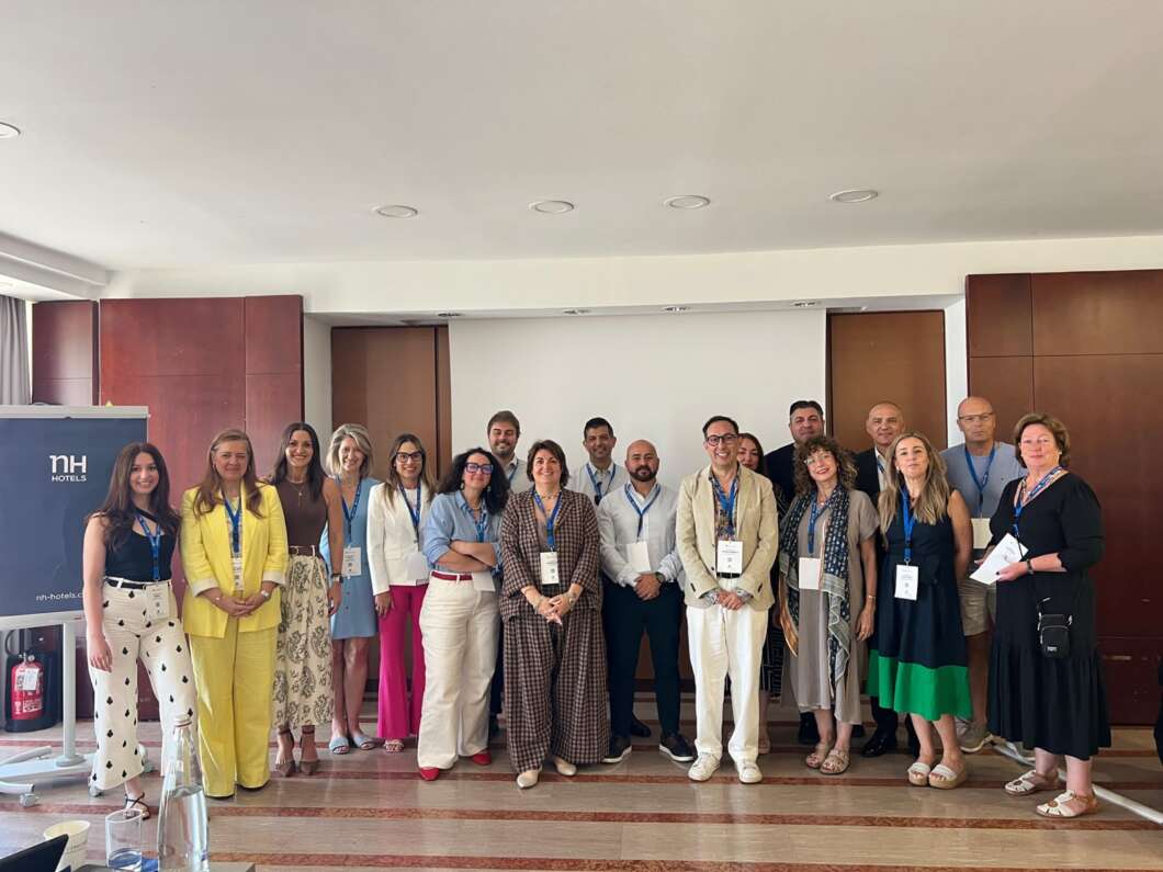 Group of diverse professionals with name badges posing for a conference photo in a hotel meeting room.