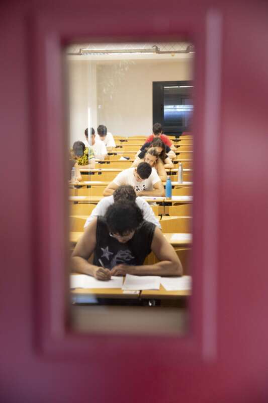 Students in a classroom taking a test, viewed through a pink-framed doorway window.