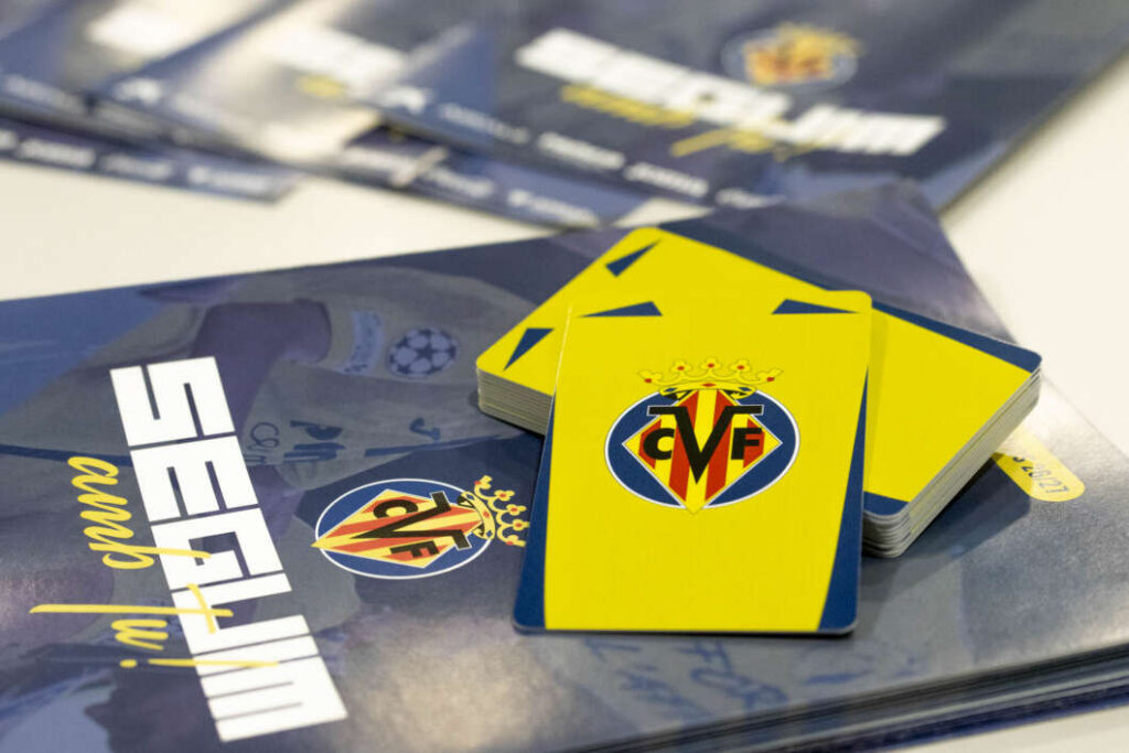 Deck of yellow cards with a club crest on top of a blue booklet or magazine surface, suggesting a sports card set.