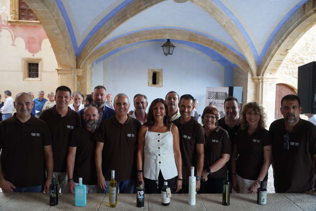 Group of people in brown shirts posing behind a stone table with bottles in a blue-arched courtyard.