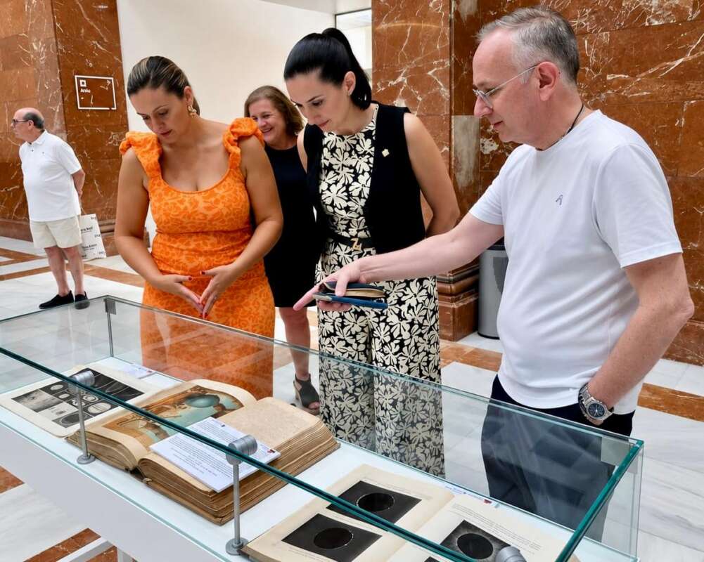 Group of four adults looking at an open, old book in a glass display case inside a museum.