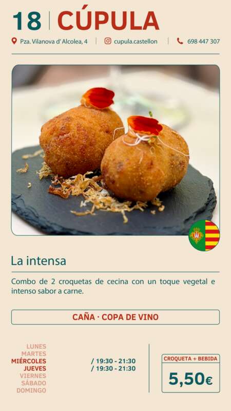 Two croquettes with a red garnish on a dark slate plate, blurred background; a small Spanish flag icon nearby.