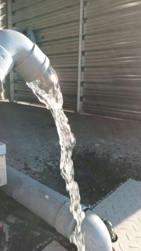 Water flowing from a curved gray pipe into a drainage area on a concrete surface outdoors